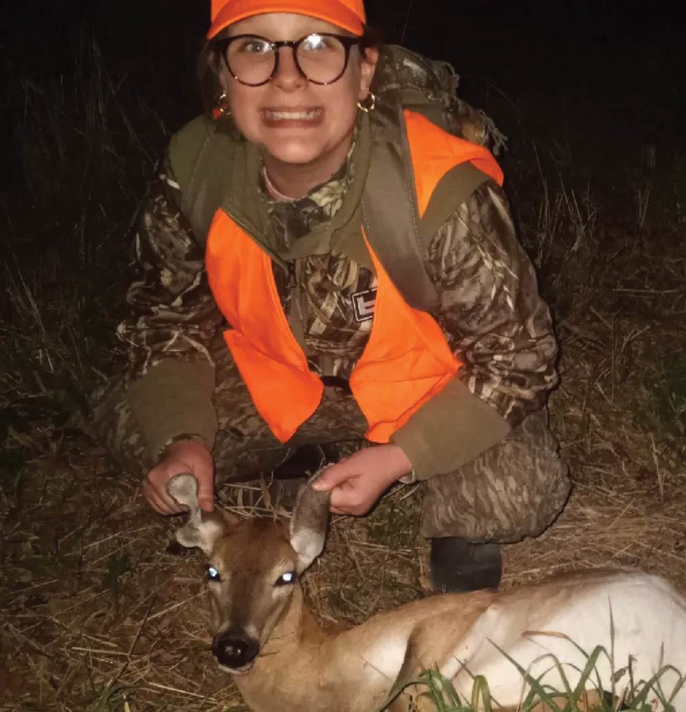 A girl smiling while posing with a hunted deer