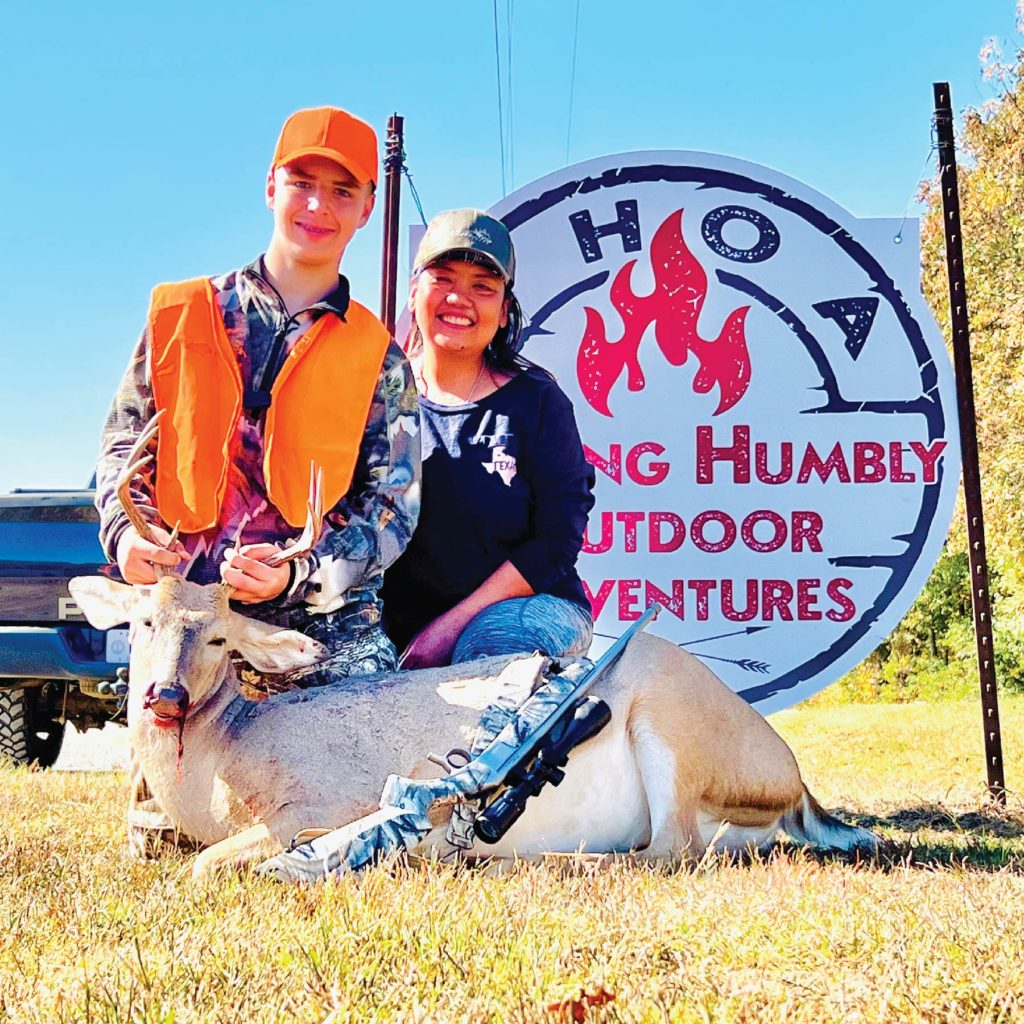 a mother and son posing with a hunted deer in front of a WHOA sign